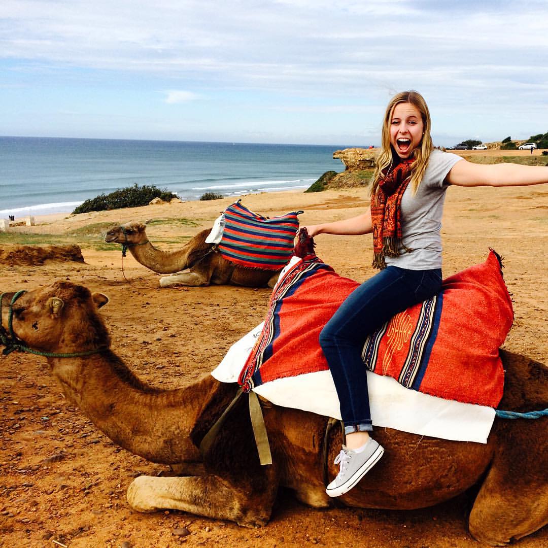 Woman sitting on a camel near the ocean smiling